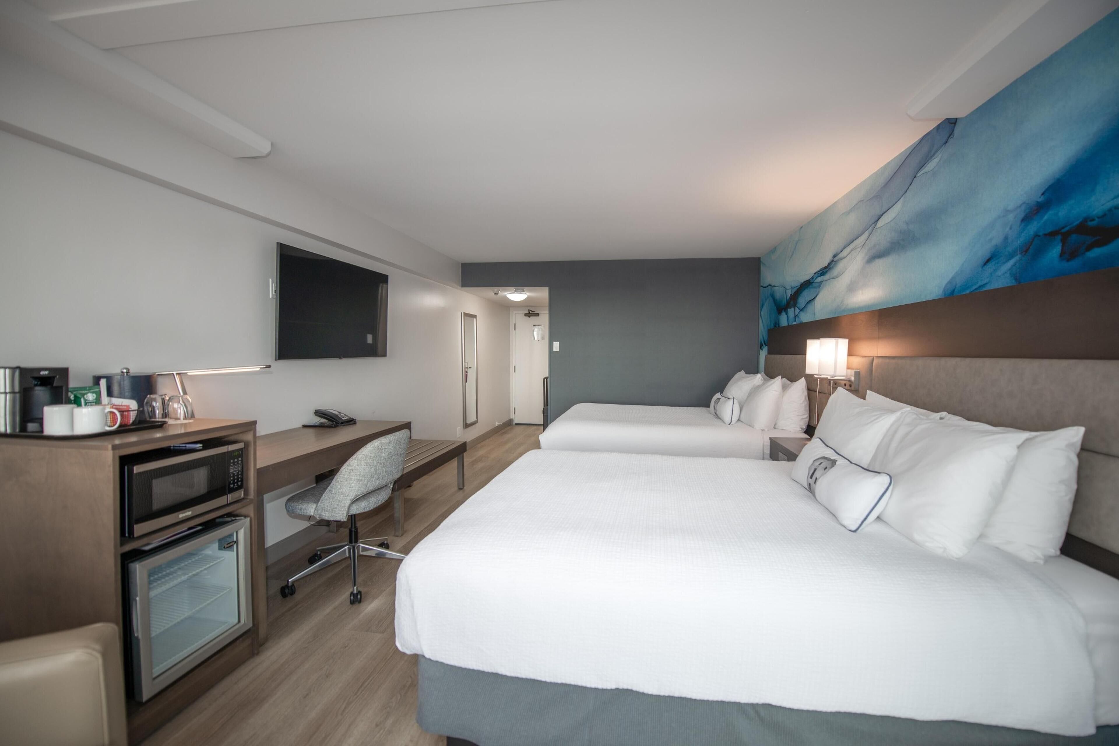 Habitación de hotel con una cama grande, un escritorio con microondas, una silla y un televisor montado en la pared.
