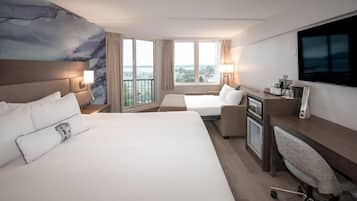 A hotel room with a large bed, a desk with a chair, a TV, and a view of the city.