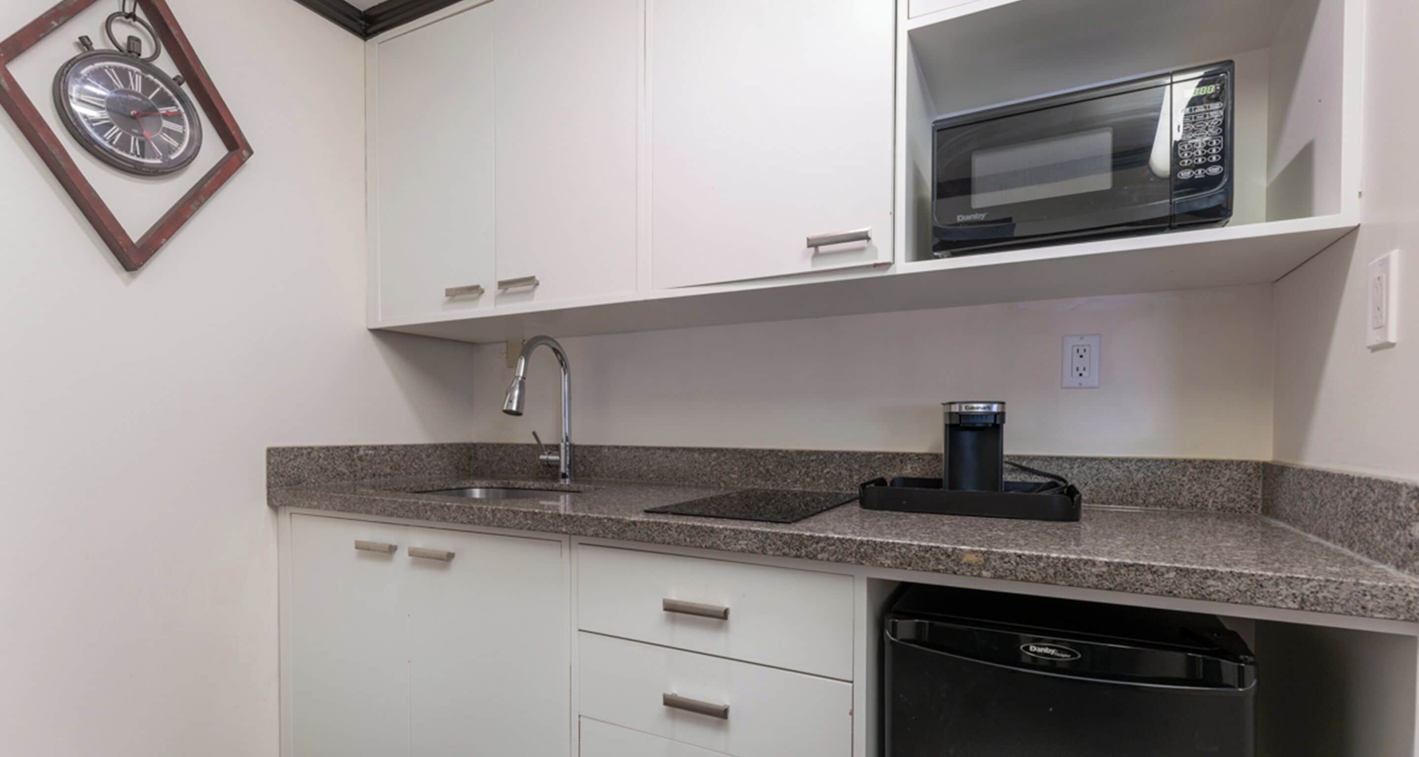 A kitchen with white cabinets, a granite countertop, a built-in microwave, a coffee maker, and a dishwasher.