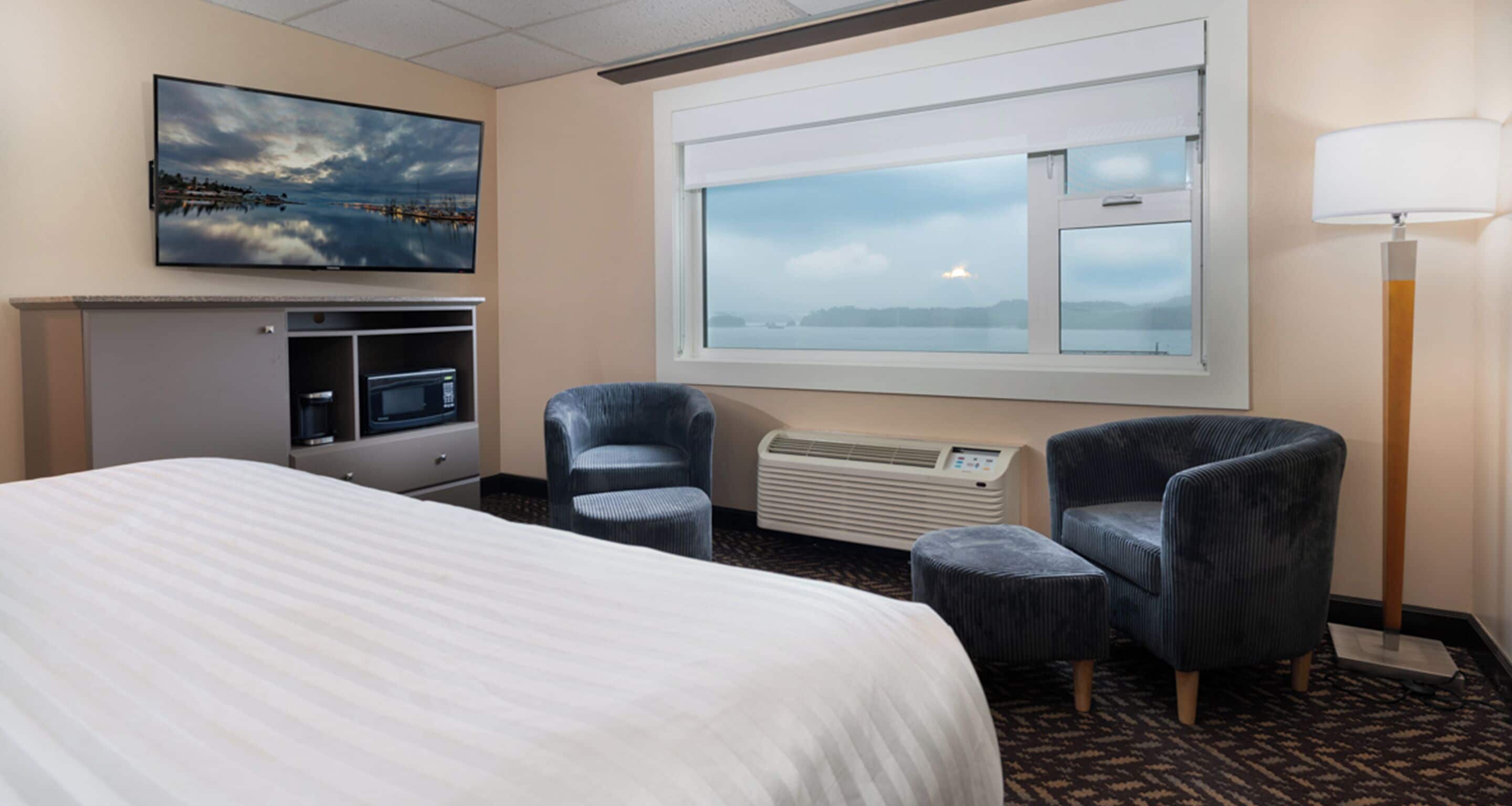 Une chambre d’hôtel comprenant un lit, un bureau avec un ordinateur, deux fauteuils, une fenêtre avec vue et un téléviseur à écran plat fixé au mur.