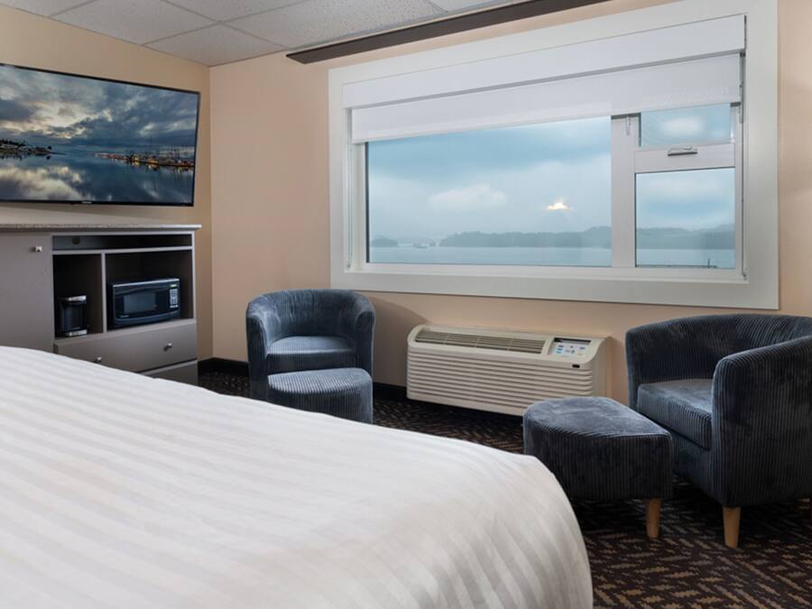 Une chambre d’hôtel comprenant un lit, un bureau avec un ordinateur, deux fauteuils, une fenêtre avec vue et un téléviseur à écran plat fixé au mur.