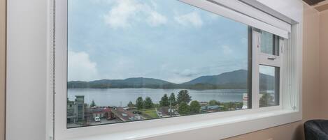 A room with a large window overlooking a lake and mountains.