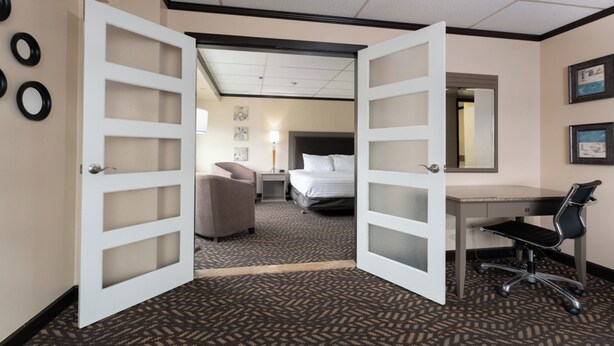 Habitación de hotel con puerta abierta que da a un dormitorio, un escritorio, una silla y una cama.