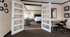 A hotel room with an open door leading to a bedroom, a desk, a chair, and a bed. - Prestige Oceanview Hotel Prince Rupert (Prince Rupert)