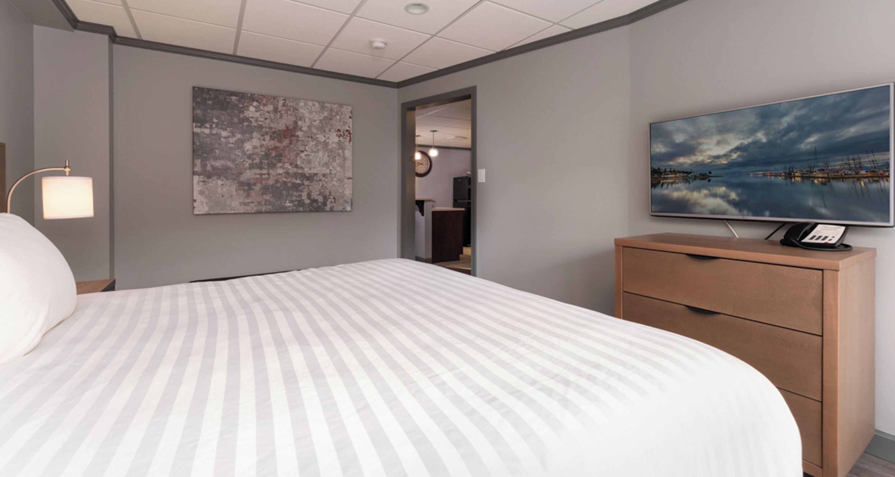 A hotel room with a large bed, a wooden dresser, a flat-screen TV, and a painting on the wall.