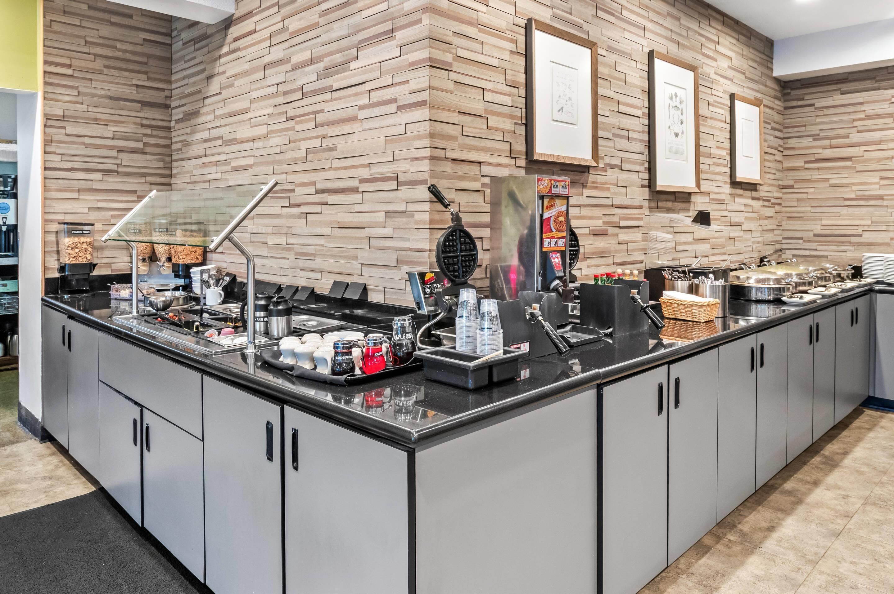 A buffet setup with a brick wall background, a coffee station, and various food containers.