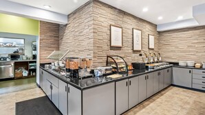 Una cocina moderna con pared de ladrillo, un mostrador tipo buffet con diferentes alimentos y una estación de café.