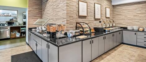 Una cocina moderna con pared de ladrillo, un mostrador tipo buffet con diferentes alimentos y una estación de café.