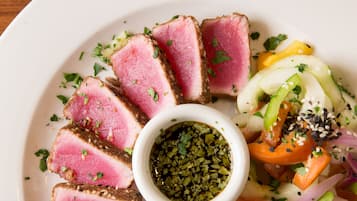 A plate of food with sliced meat, vegetables, and a small bowl of sauce.