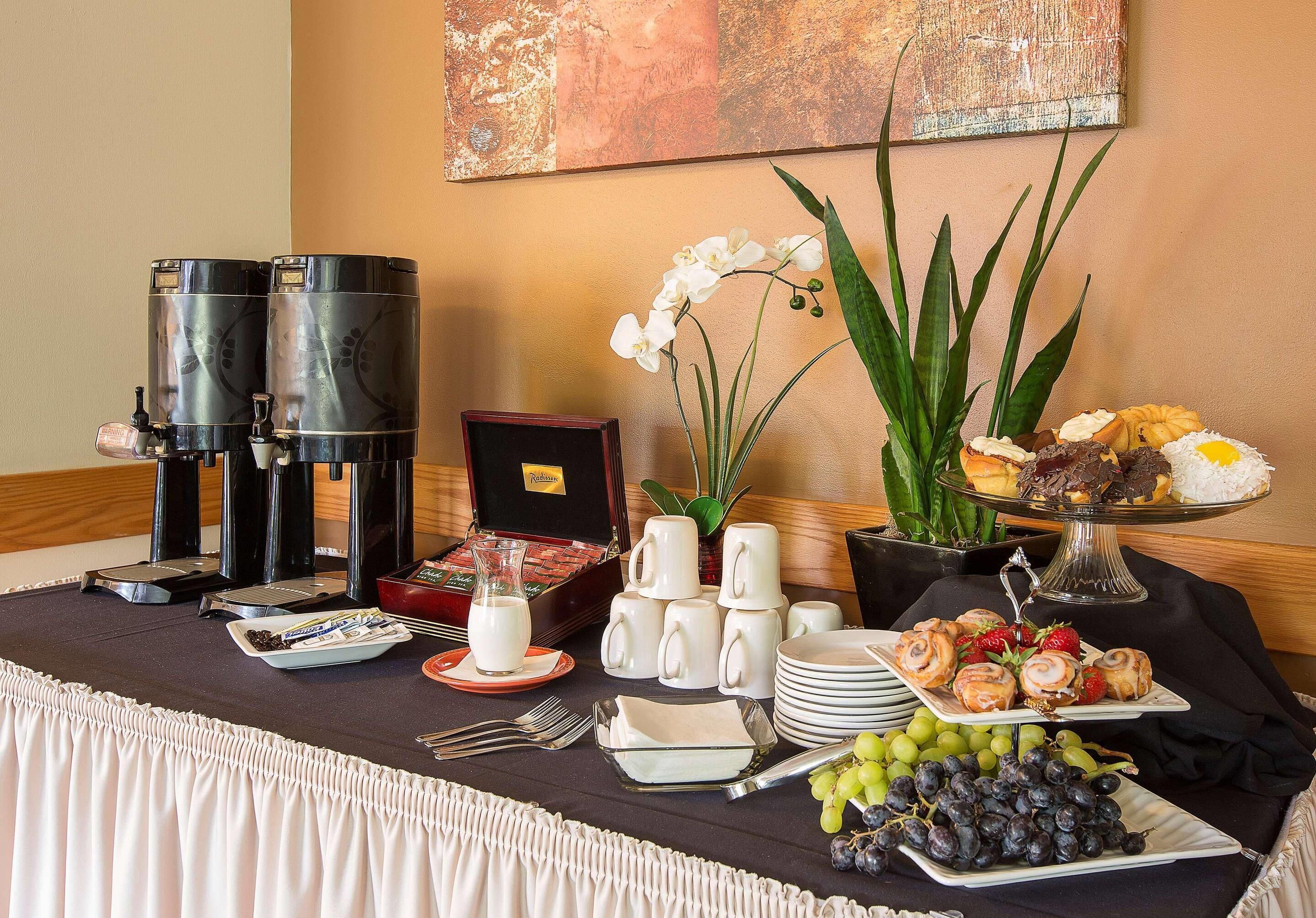 A breakfast buffet with coffee makers, a vase of orchids, and various pastries and fruits.