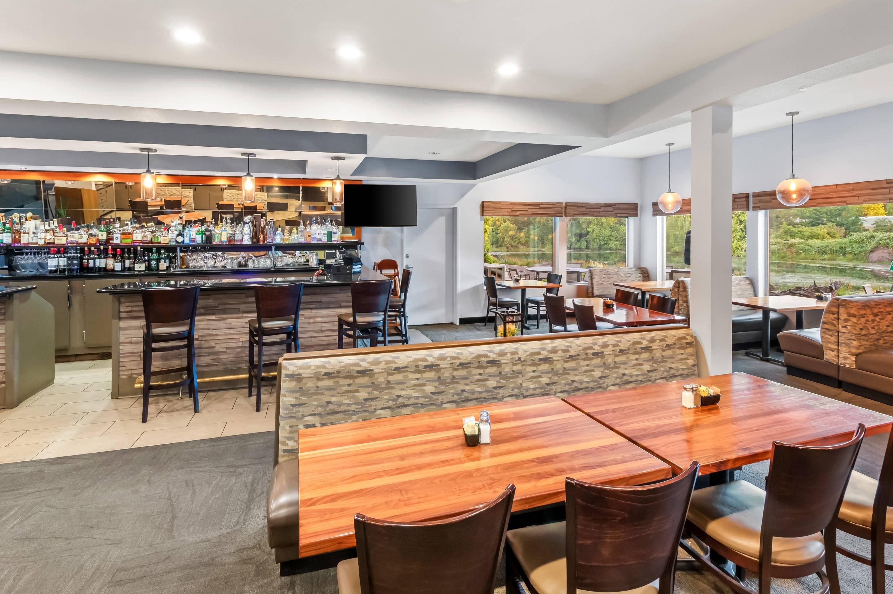 Un espace bar moderne, doté d’un assortiment de bouteilles d’alcool, d’un téléviseur à écran plat et d’un coin salon avec des tables et des chaises en bois.