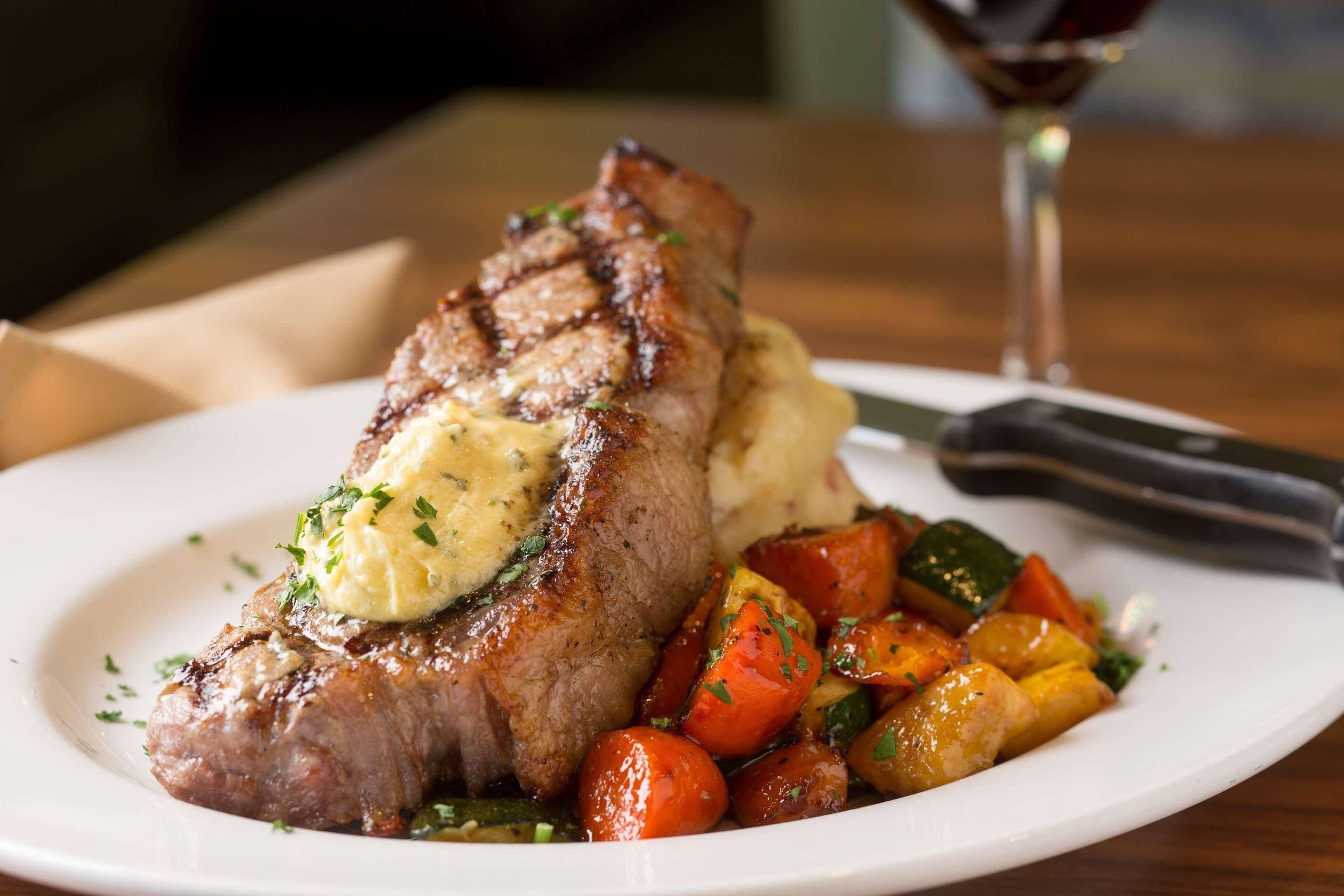A plate of steak with a pat of butter and roasted vegetables.