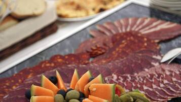 Una mesa de buffet con diversos alimentos, incluyendo carnes cortadas, frutas y verduras.