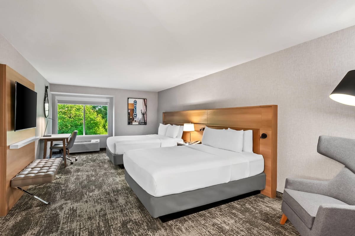 A hotel room with two beds, a desk, a chair, and a TV.