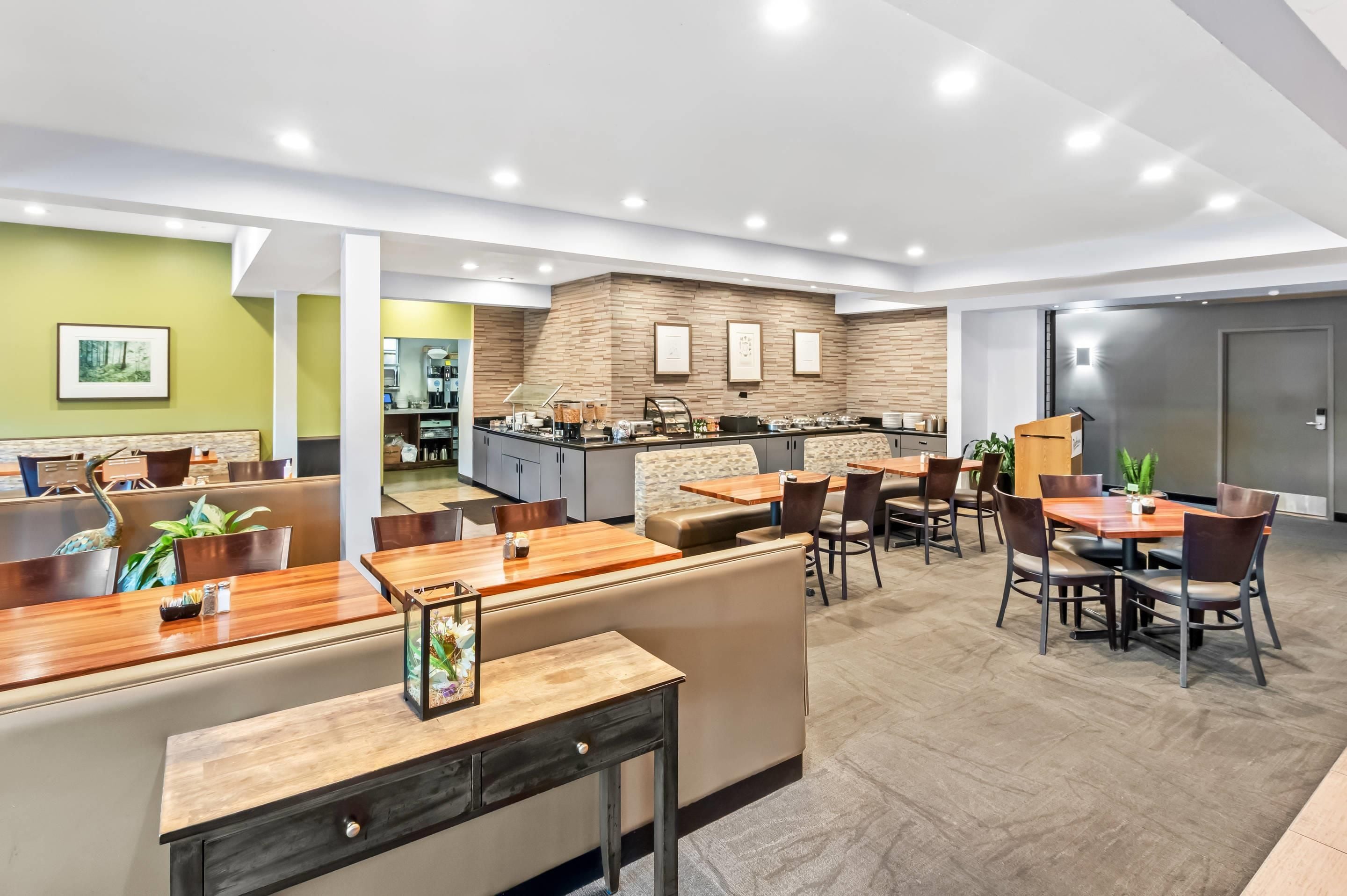 A modern hotel lobby with a reception desk, seating area, and a kitchen in the background.