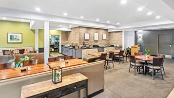 A modern hotel lobby with a reception desk, seating area, and a kitchen in the background.
