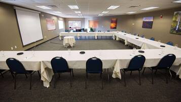 A conference room with long tables, chairs, a projector screen, and artwork on the walls.