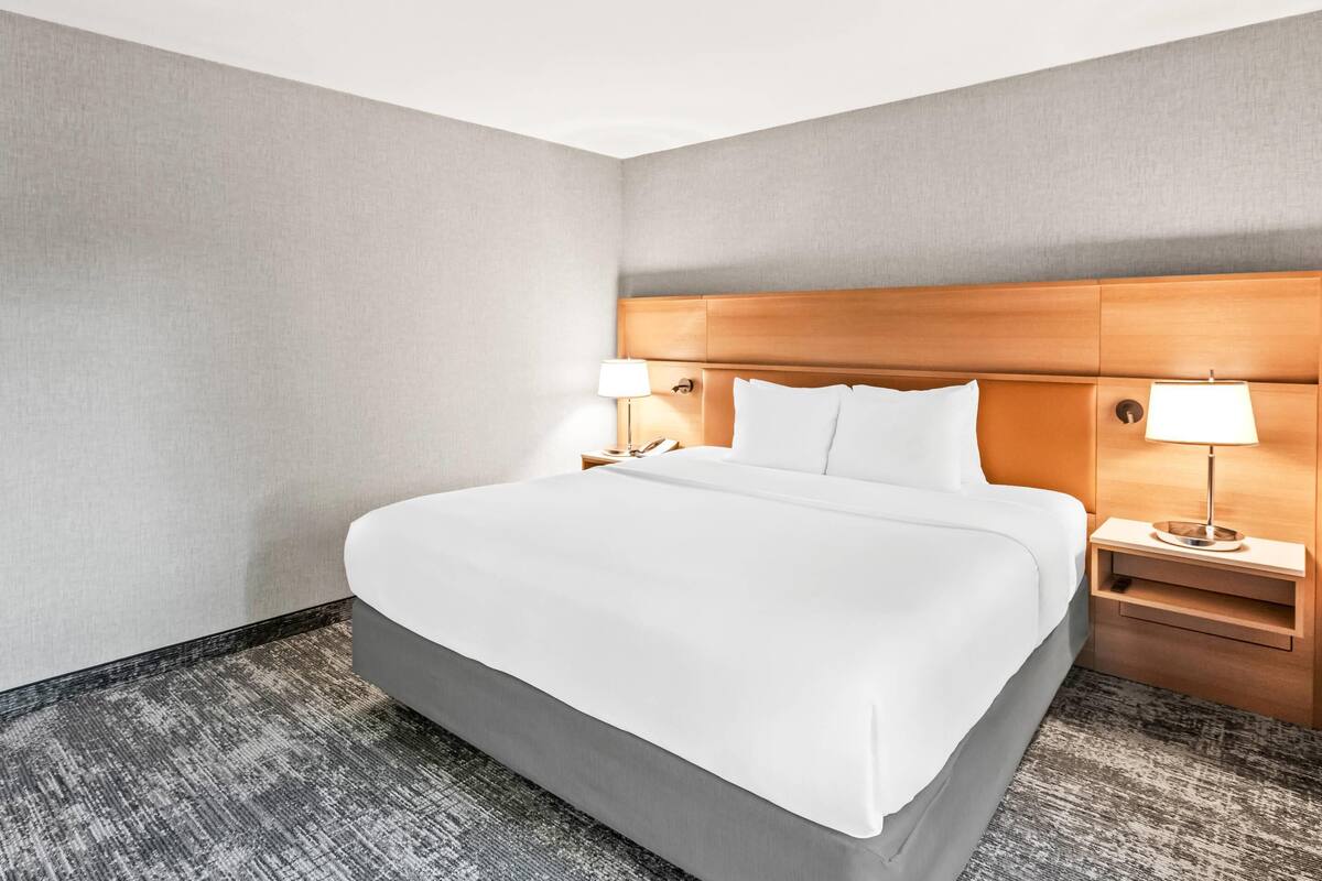 A hotel room with a large bed, two bedside tables with lamps, and a grey carpeted floor.