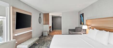 A hotel room with a large bed, a seating area, a television, and a painting on the wall.