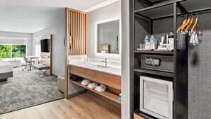 Un baño de hotel moderno con un espejo grande, ducha integrada y tocador con lavamanos y espacio de almacenamiento.