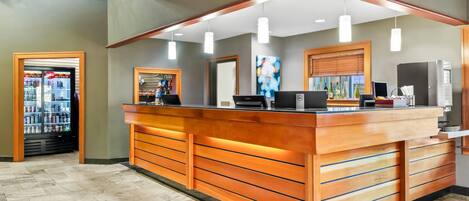 A reception desk with a wooden finish, a refrigerator, and a vending machine.