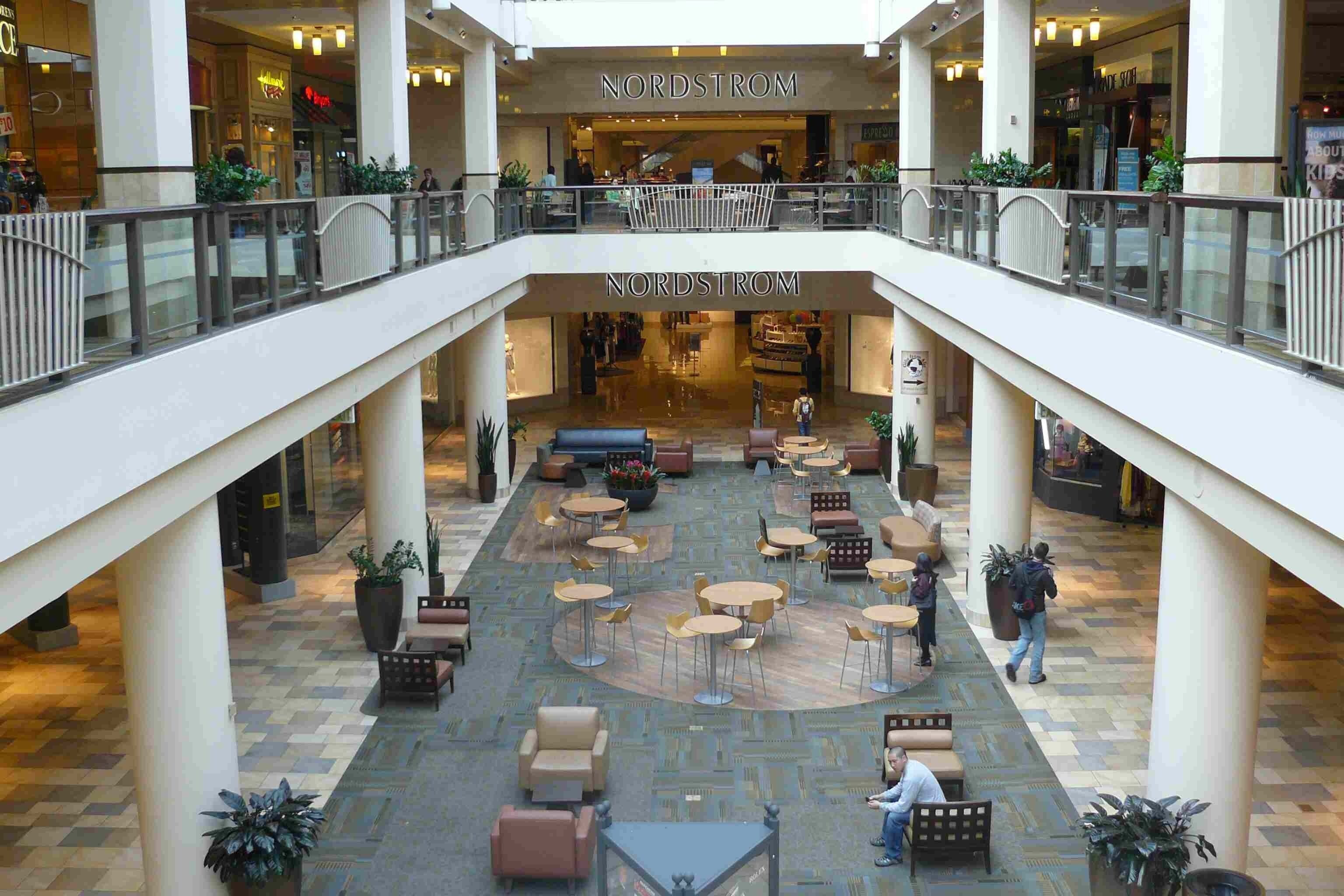 A spacious indoor atrium with multiple seating areas, a central coffee shop, and a visible staircase leading to an upper level.