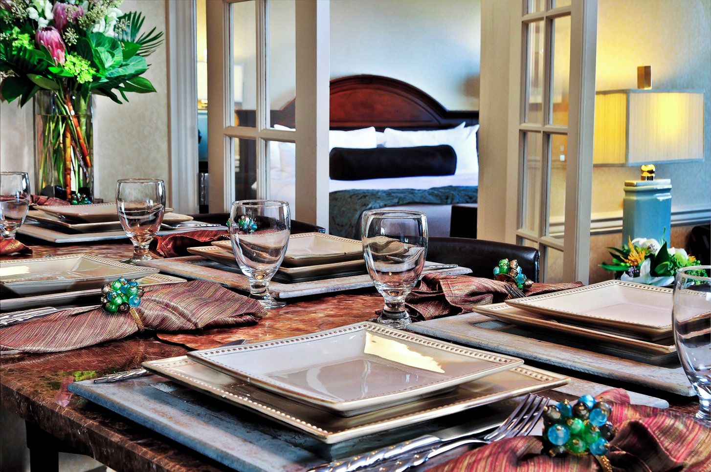 A dining table set with plates, glasses, and cutlery, with a vase of flowers on the left.
