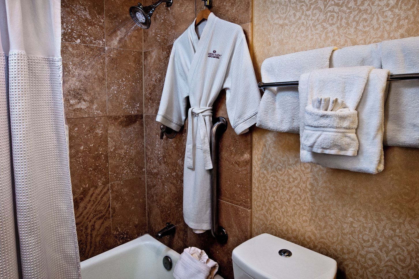 A bathroom with a bathtub, a toilet, a shower with a handheld showerhead, and a towel rack with multiple towels.