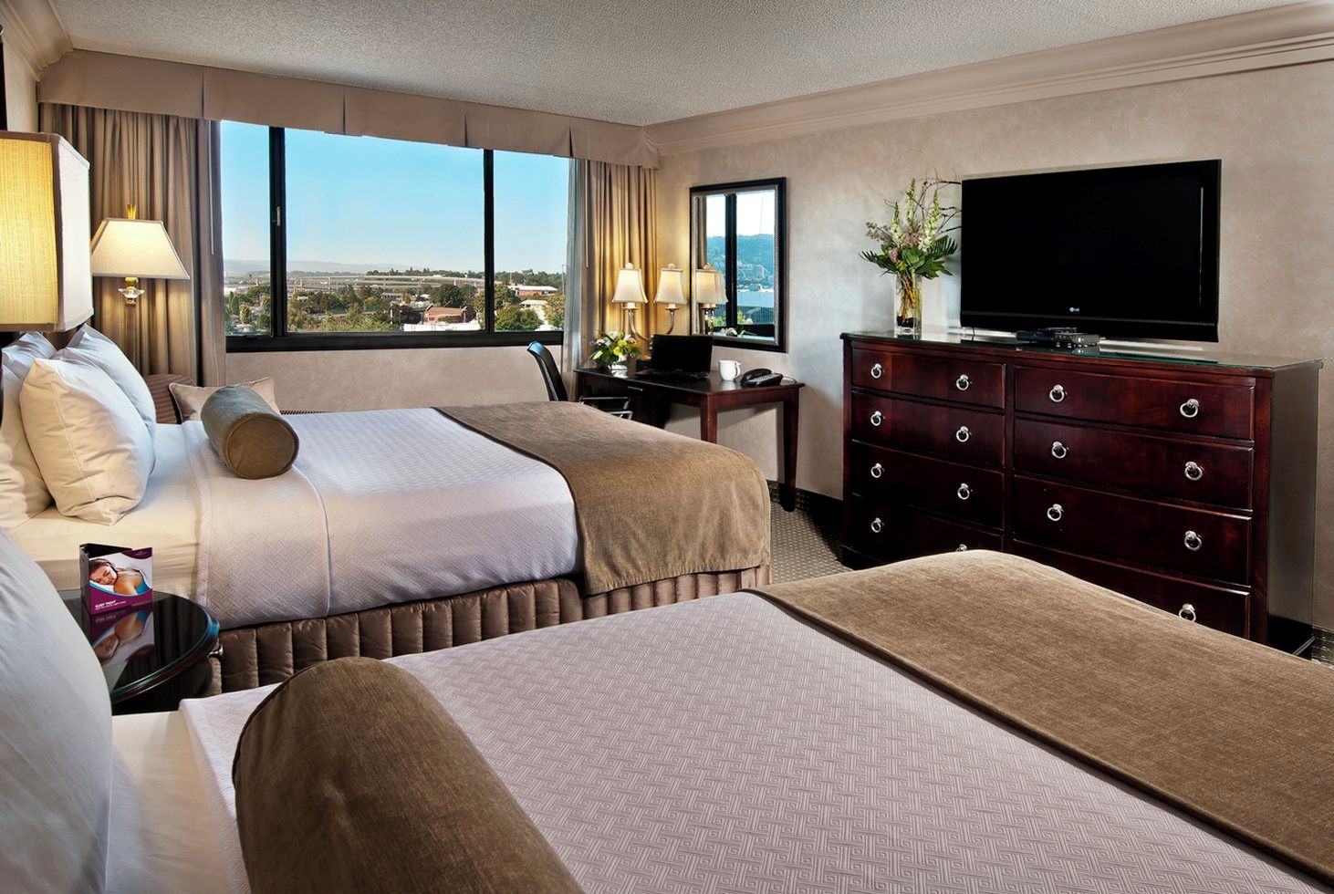 A hotel room with two beds, a television, a dresser, and a view of the city.