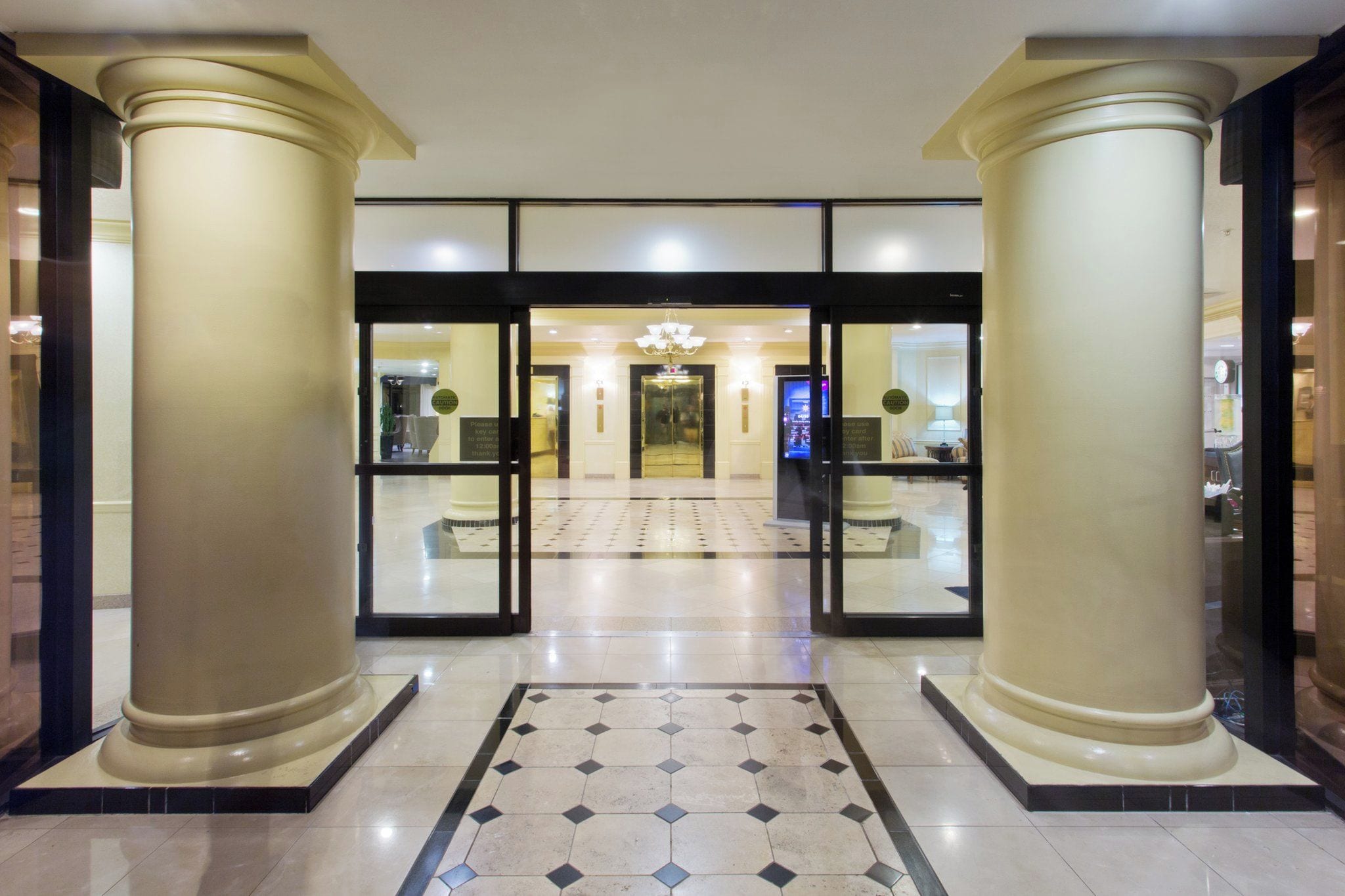 A hotel lobby with a central chandelier, a reception desk, and a check-in counter.