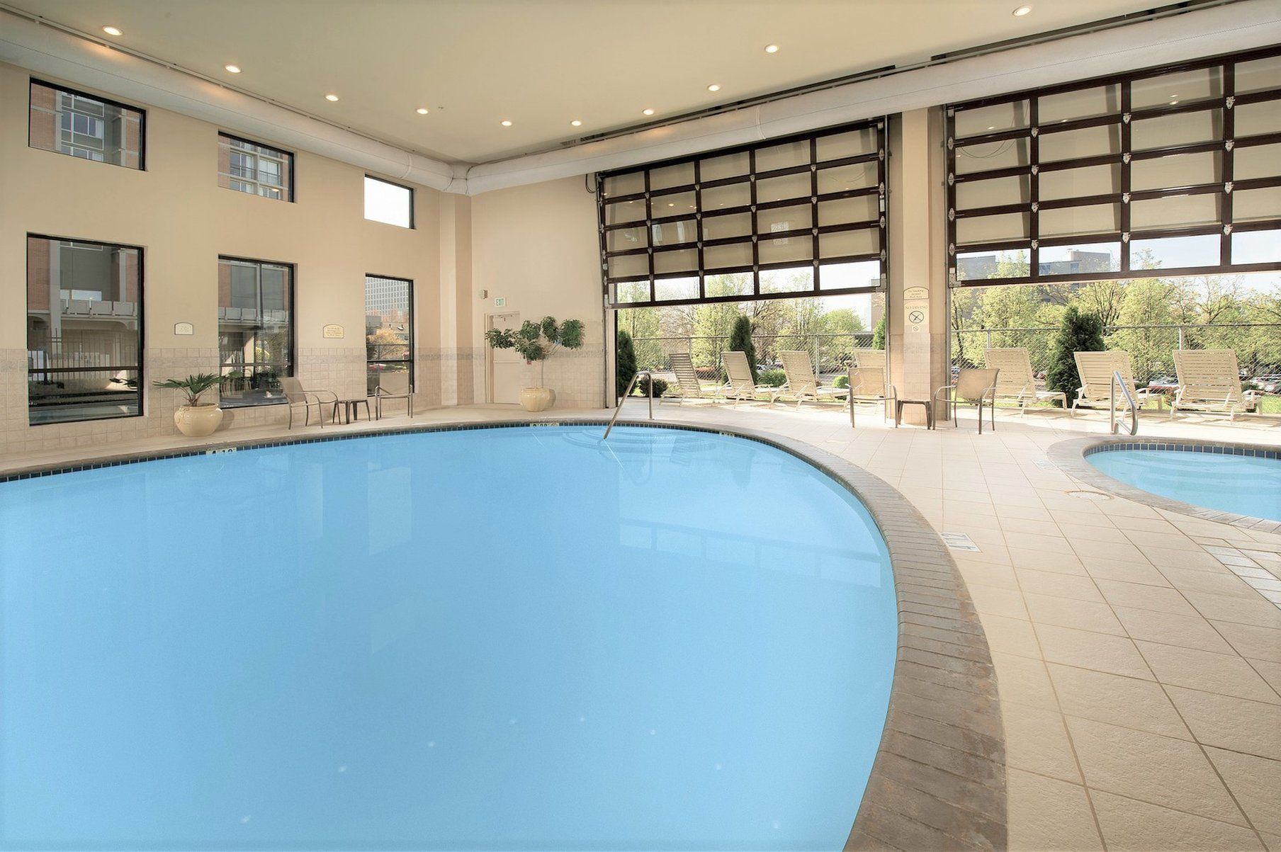 Una piscina con solárium alicatado, sillas de descanso y amplias ventanas.