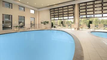 Una piscina con solárium alicatado, sillas de descanso y amplias ventanas.