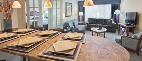 A hotel room with a dining area, a living room, and a bedroom.