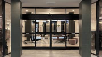 Un vestíbulo de hotel con puerta de cristal, mostrador de recepción y zona de estar.