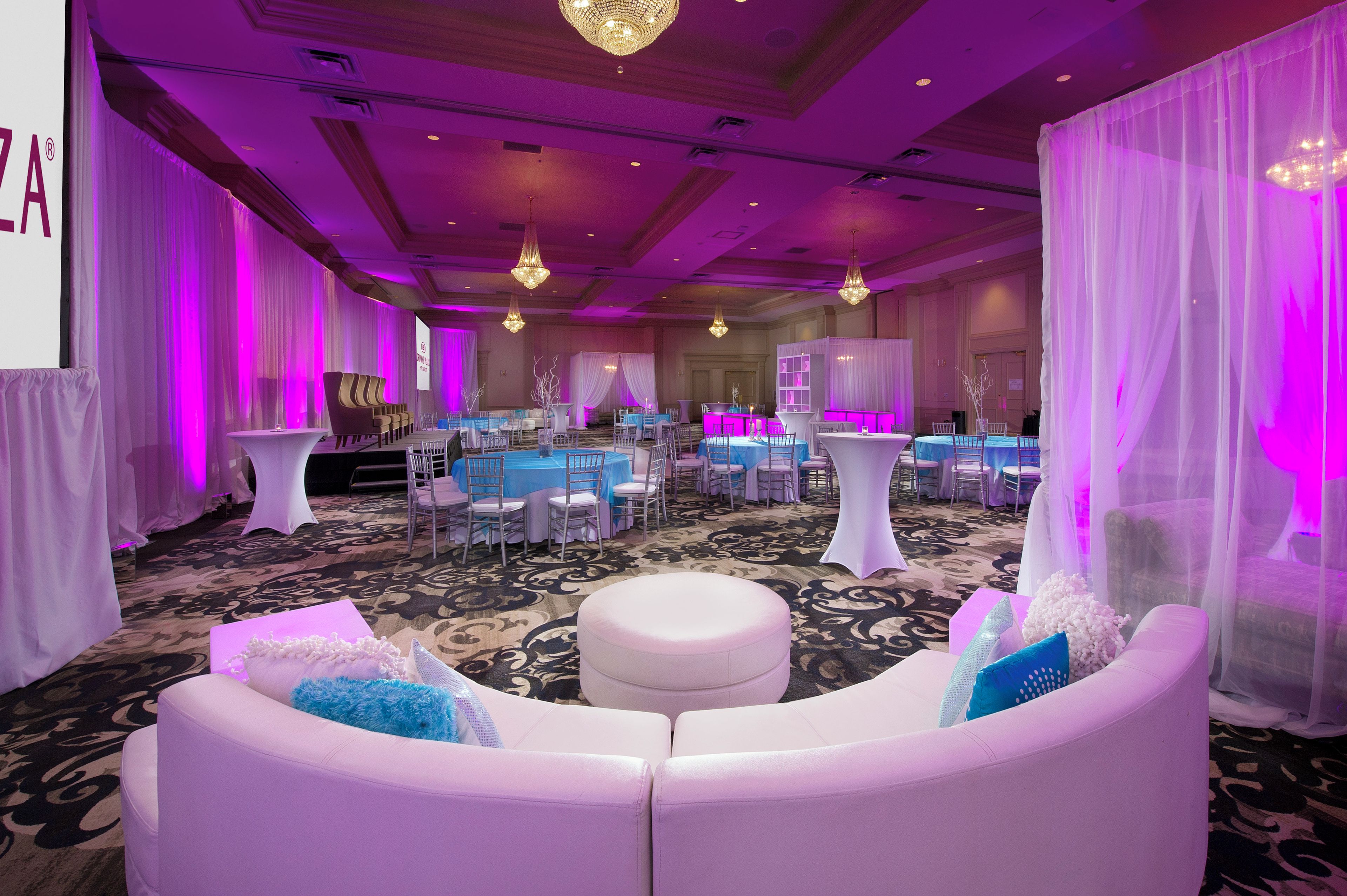 Une salle de banquet avec des tables rondes, des chaises et un canapé blanc agrémenté de coussins bleus.