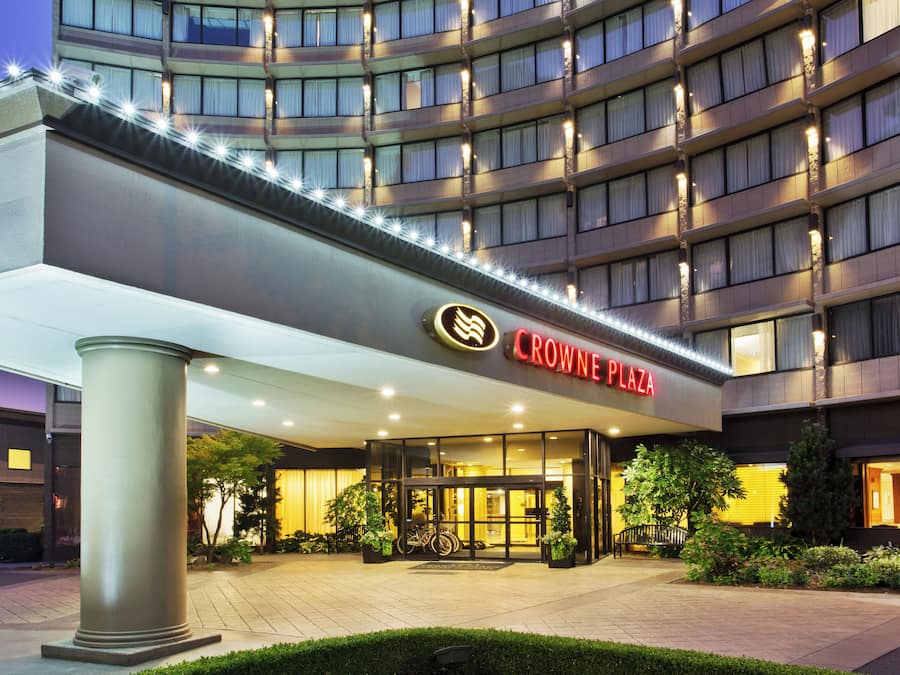 Entrada de un hotel con diseño moderno, destacándose el letrero de 'Crowne Plaza'.
