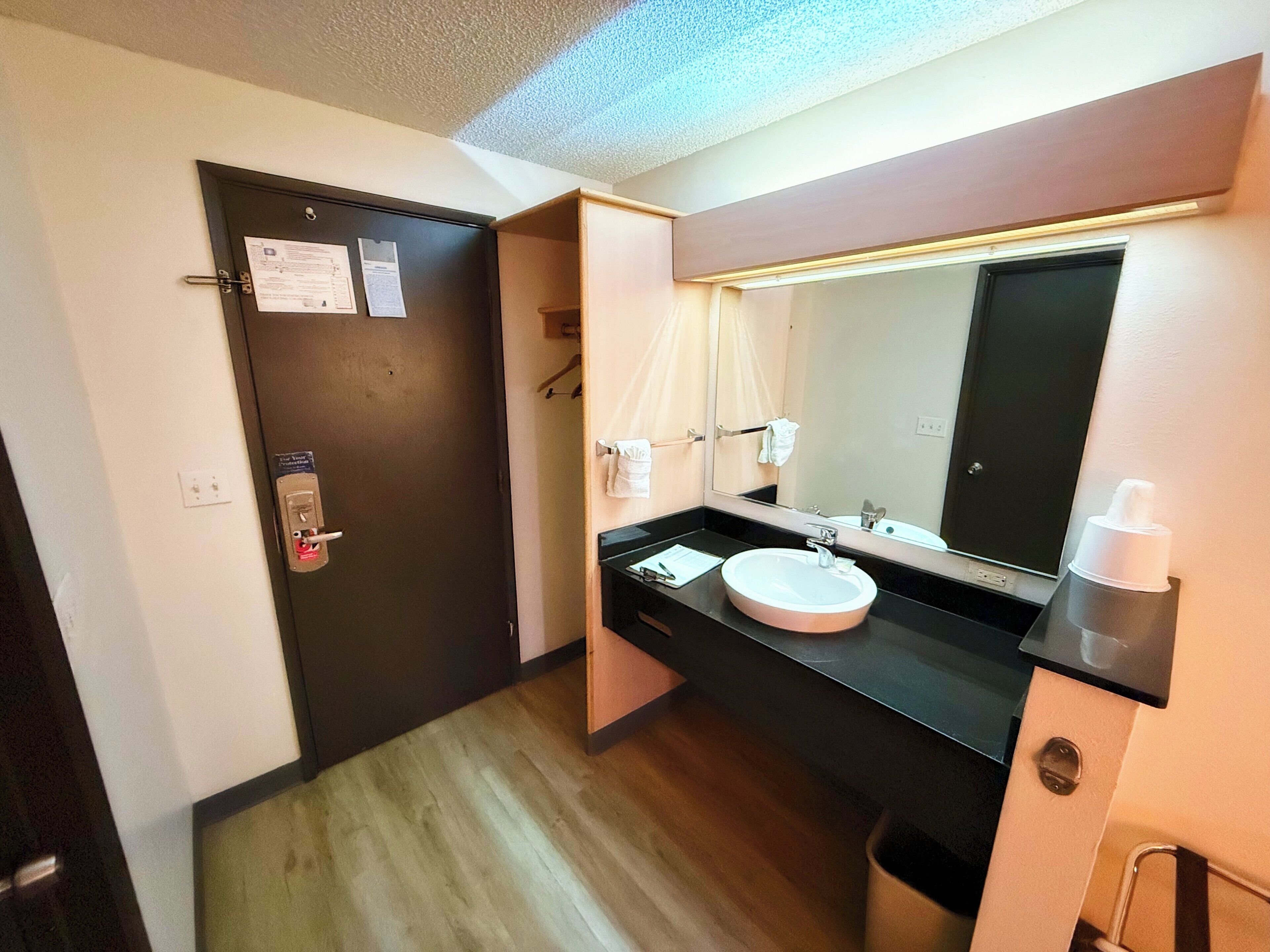 Un baño de hotel con lavamanos, espejo, toallero y una puerta con cerradura.