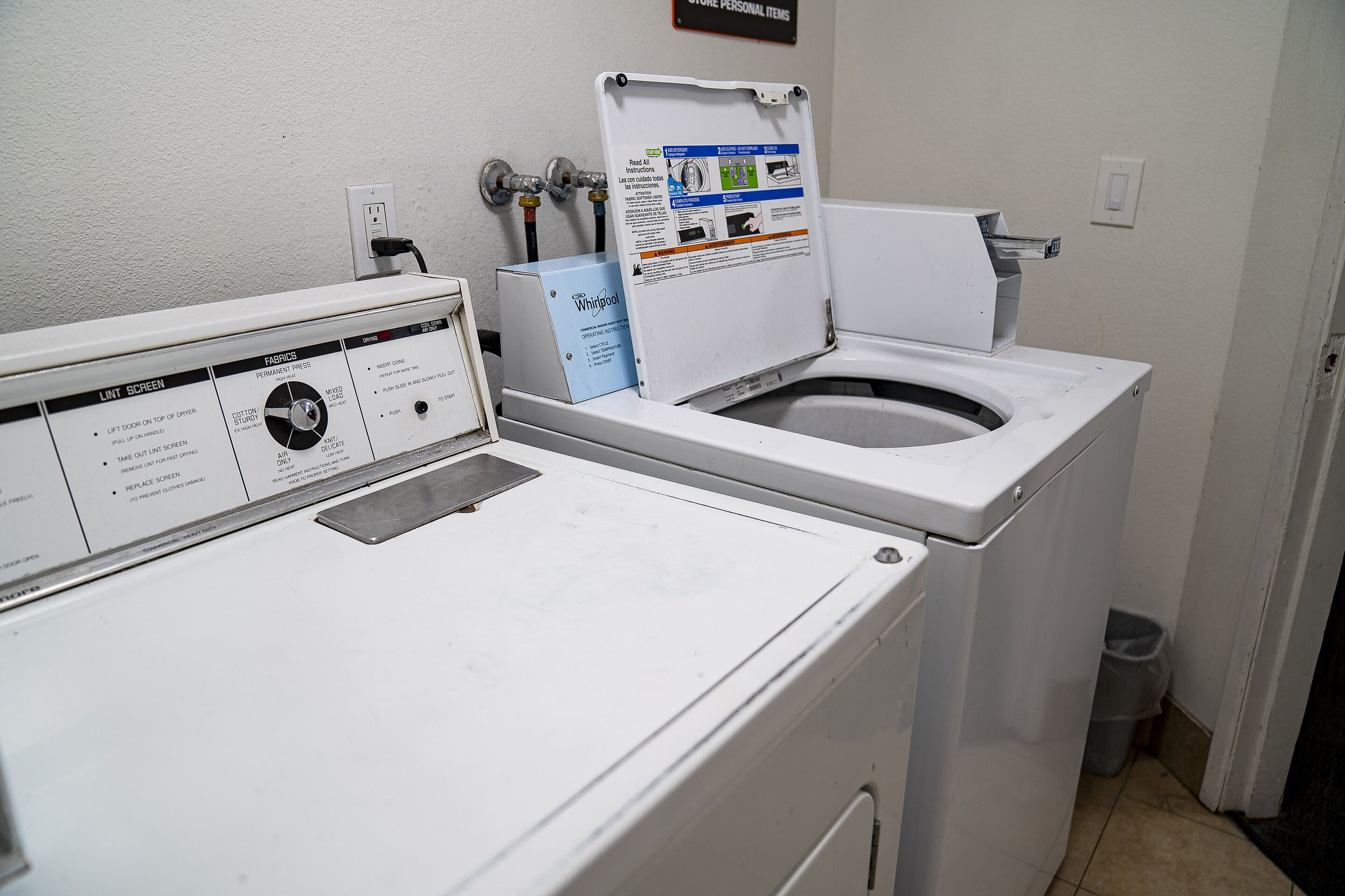 Een wasruimte met een voorlader wasmachine en droger, een bedieningspaneel en een bordje met de tekst 'LIFT SCREEN'.