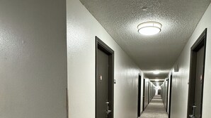 A long, narrow hallway with doors on both sides, carpeted floor, and a ceiling light.