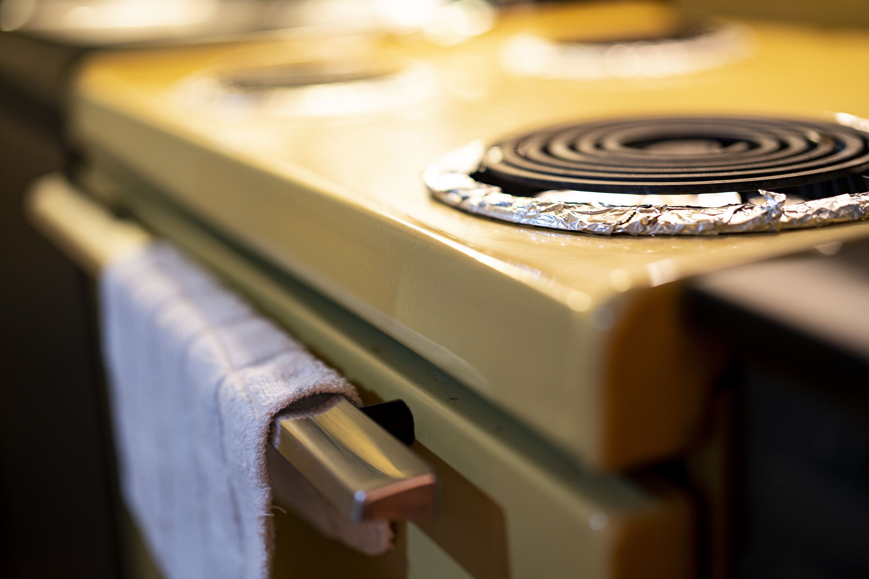 A close-up of a kitchen stove with a metallic knob and a towel hanging on the side.