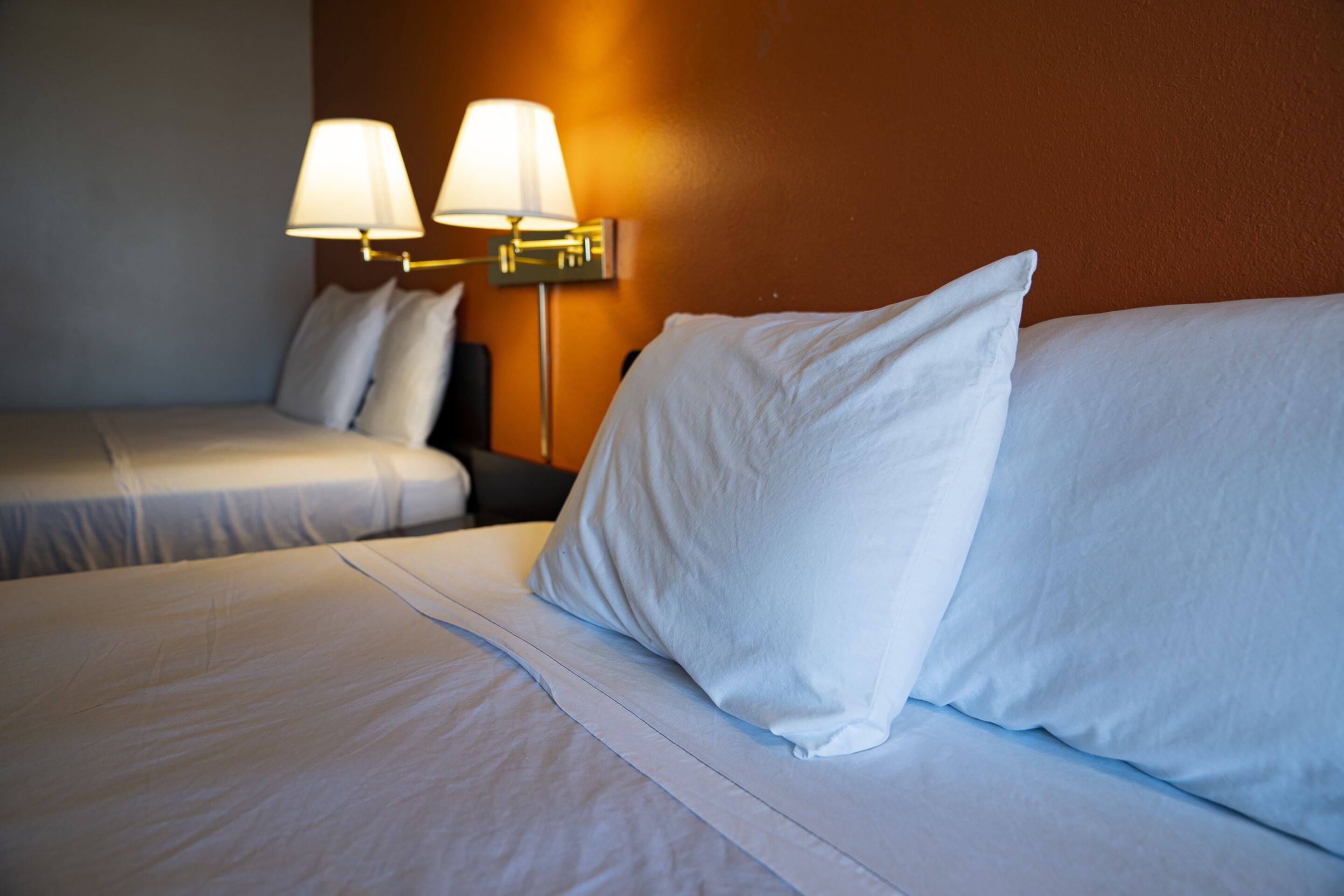 Une chambre d’hôtel avec deux lits, chacun étant équipé de draps et d’oreillers blancs. On y trouve deux lampes fixées au mur, dotées d’abat-jours blancs.