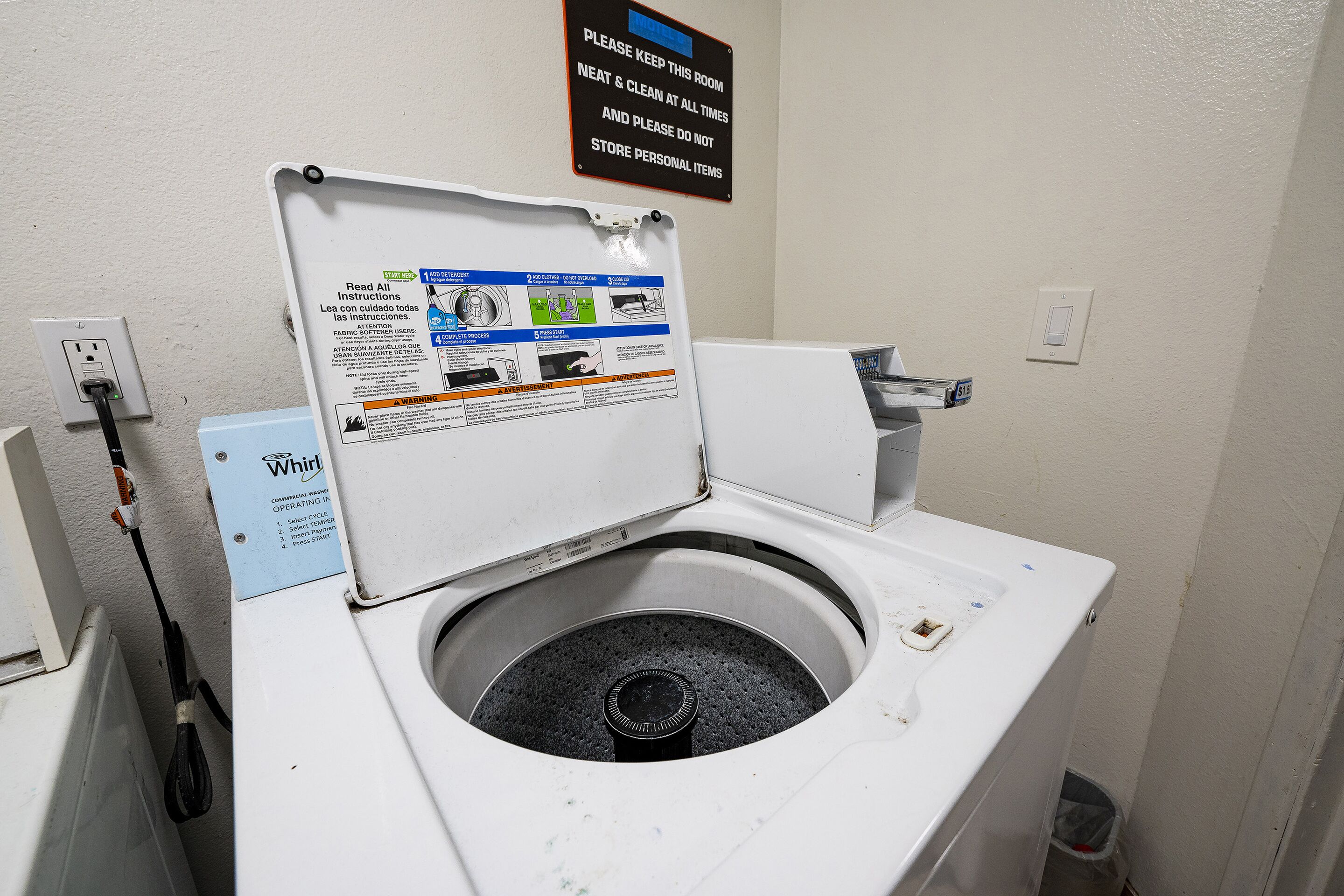 Eine weiße, gewerbliche Whirlpool Waschmaschine mit Frontlader, einer Bedienblende mit Anweisungen und einem an einer Steckdose angeschlossenen Stromkabel.