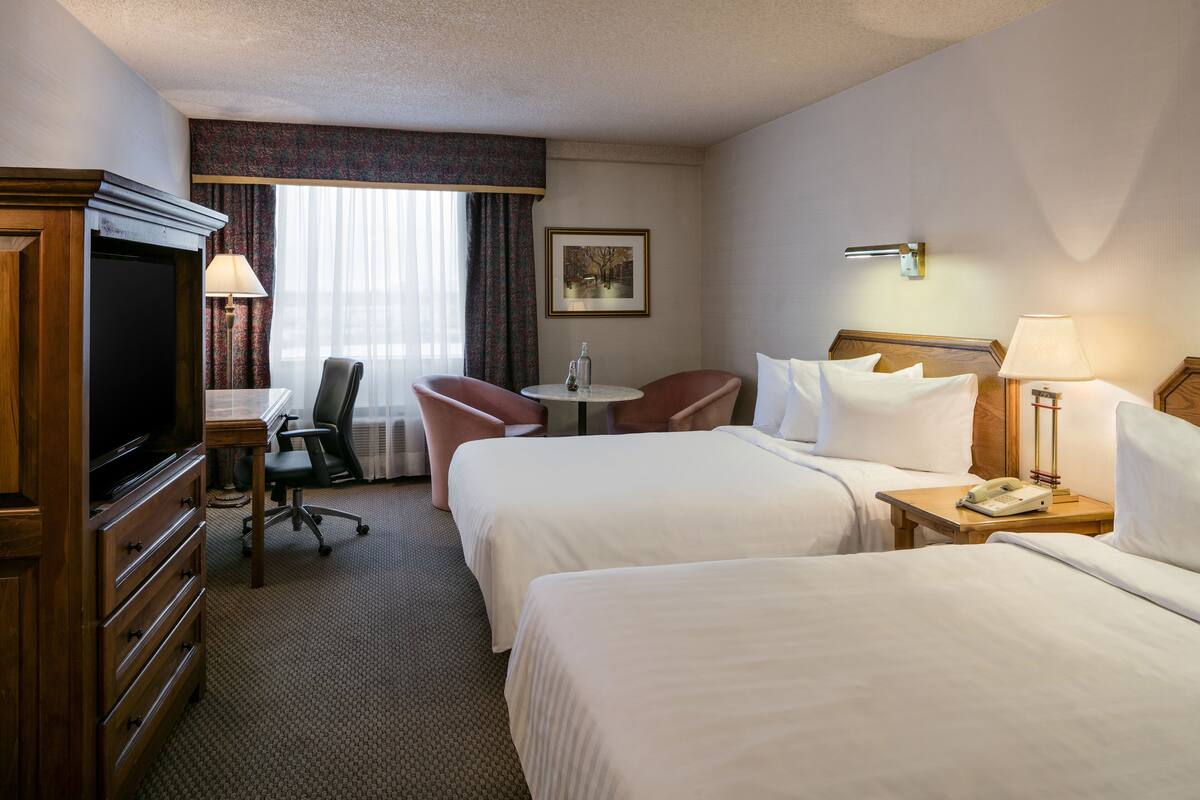 Habitación de hotel con dos camas, un escritorio, una silla, un televisor y una lámpara.