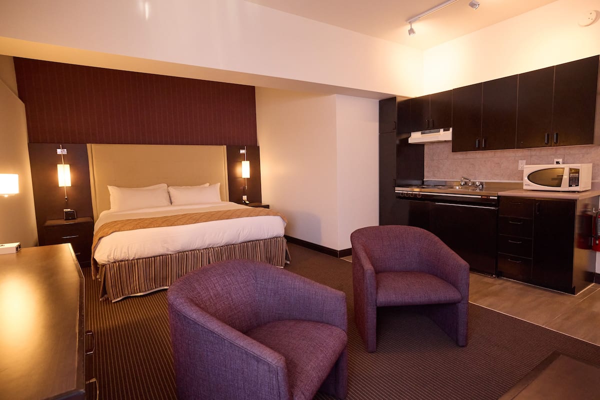 Une chambre d’hôtel comprenant un lit, deux fauteuils, un bureau, un four à micro-ondes et une kitchenette.