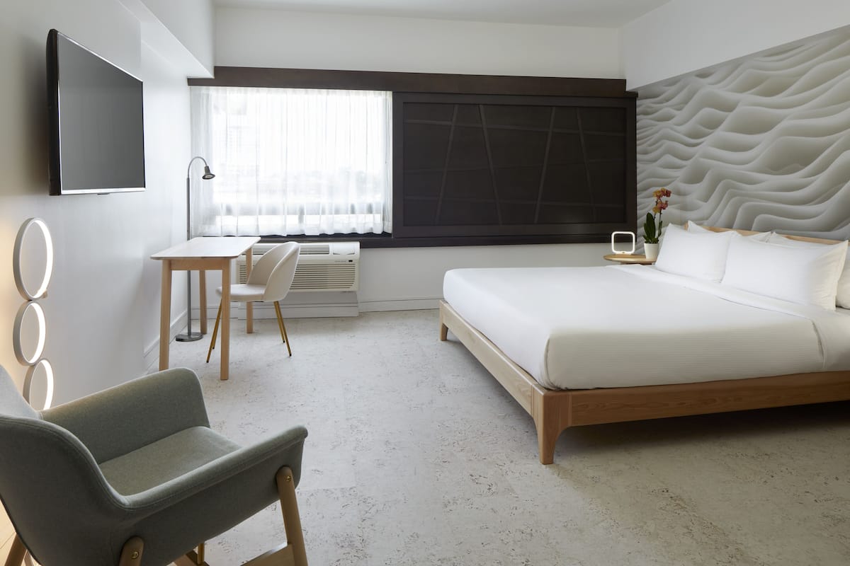Une chambre d’hôtel moderne dotée d’un grand lit, d’un bureau avec une chaise, d’un téléviseur à écran plat et d’une grande fenêtre avec des rideaux.