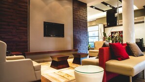A modern living room with a sofa, armchair, and coffee table. There is a flat-screen TV mounted on the wall and a decorative plant in the corner.