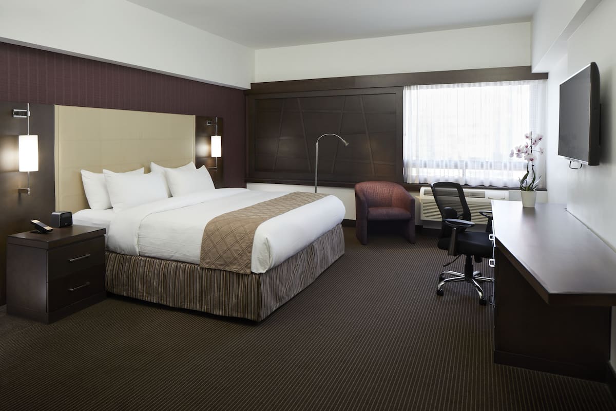 Une chambre d’hôtel avec un grand lit, un bureau, une chaise, une télévision et une fenêtre avec des rideaux.