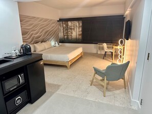 A modern bedroom with a bed, a desk with a coffee maker, a chair, and a vanity with lights.