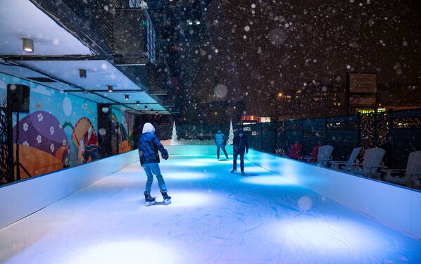 An indoor ice skating rink with a colorful mural on one wall and a snow effect.