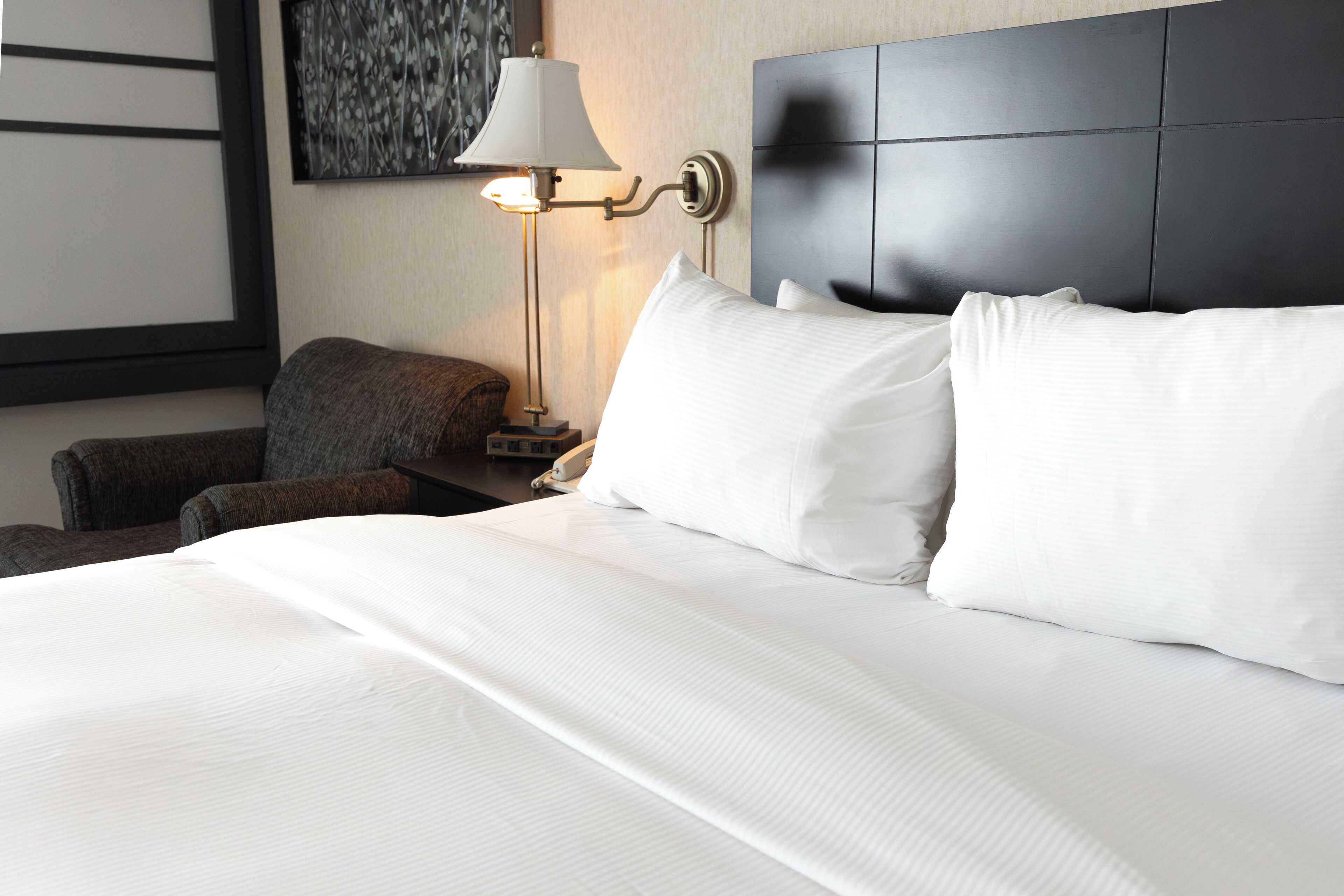 A hotel room with a large bed, a nightstand, a lamp, and a chair.